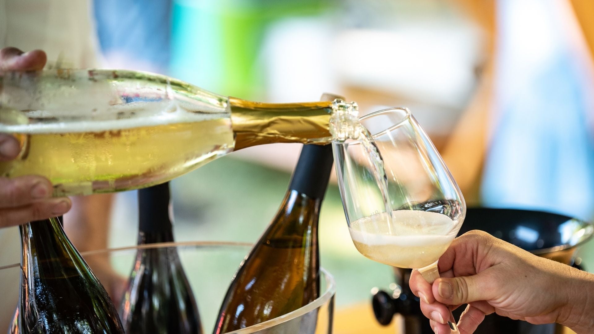 Person pouring white wine from a bottle into a glass with a blurred background