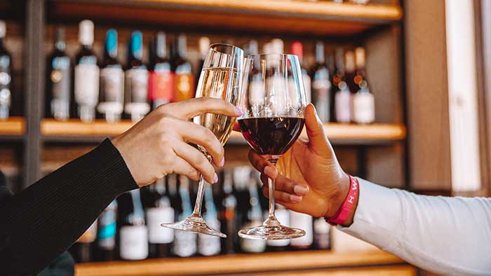 A woman and man clink their glasses in front of wine shop shelves