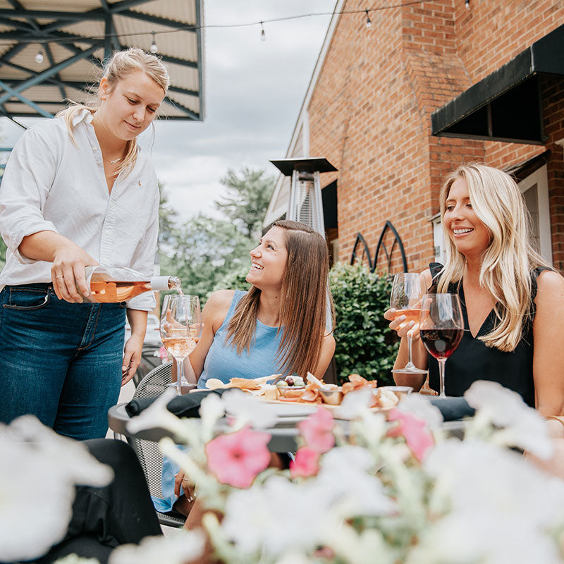A server pouring rose for a guest seated at an outdoor table