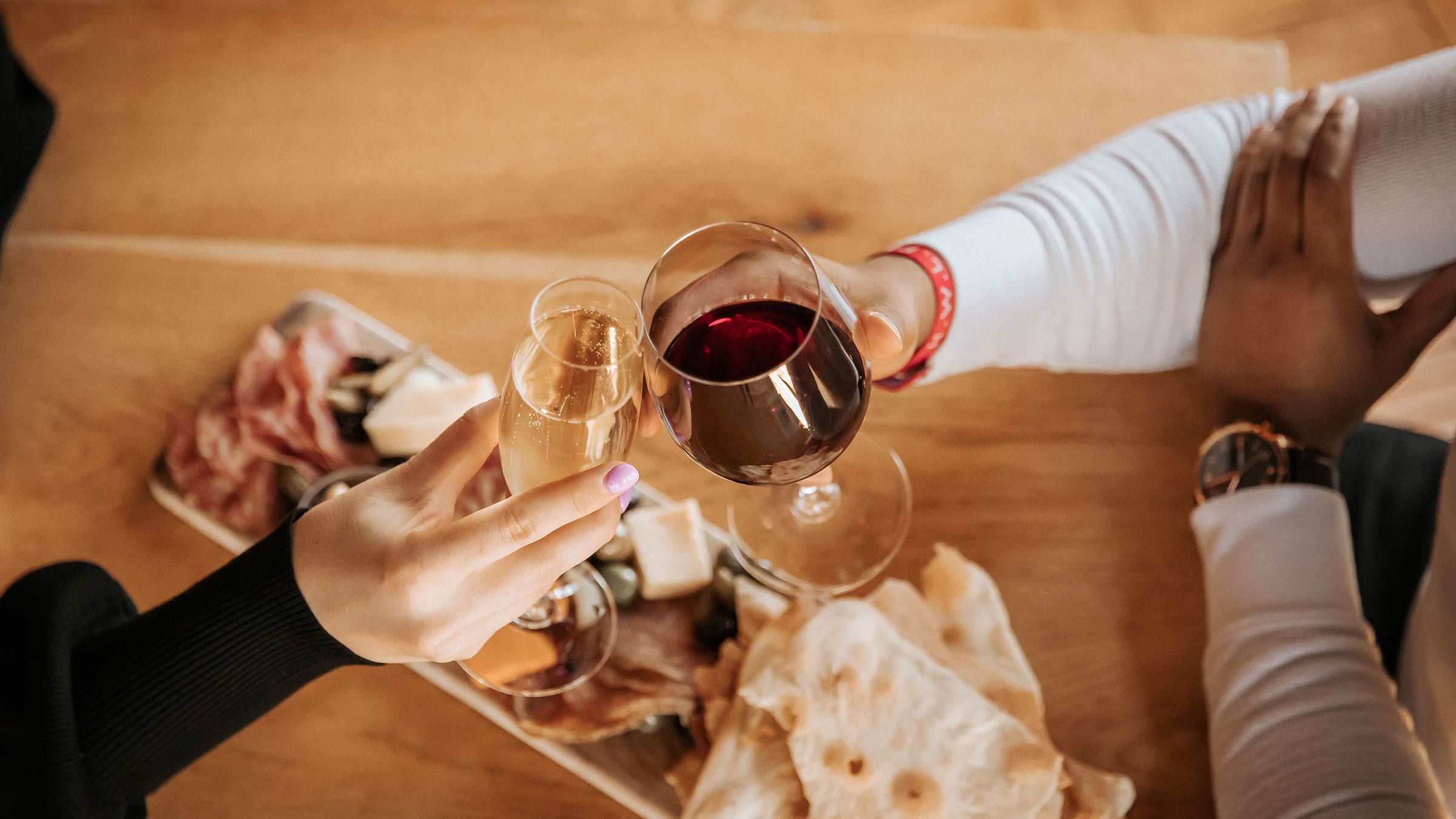 A woman and man clinking a glass of bubbly and red wine above a charcuterie board