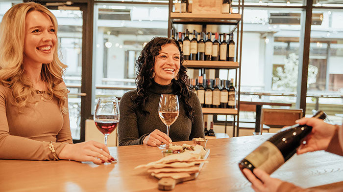 Tasting host showcasing a bottle of wine for two customers at the bar