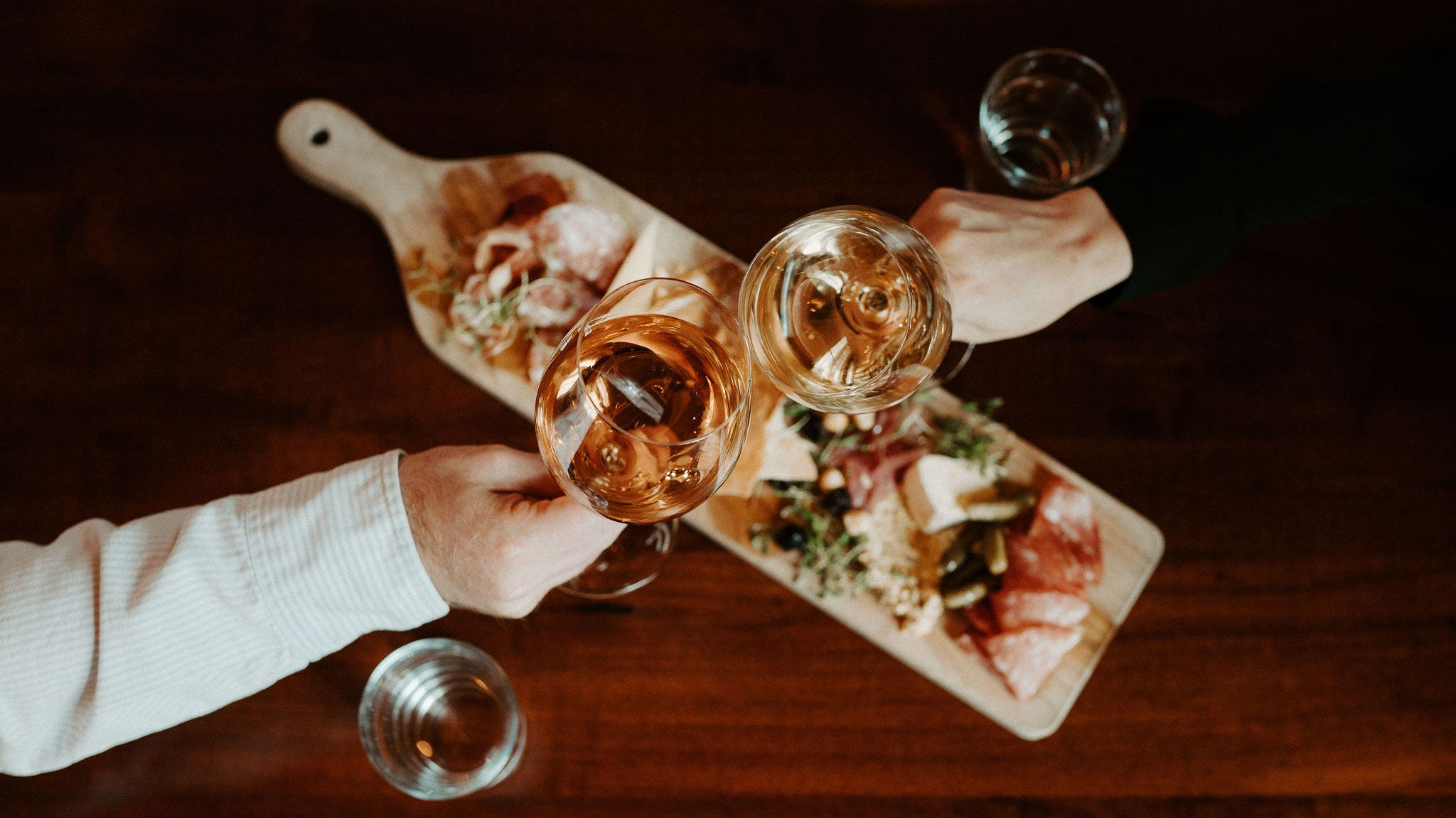 Two customers clinking their wine glasses above a cheese and charcuterie board