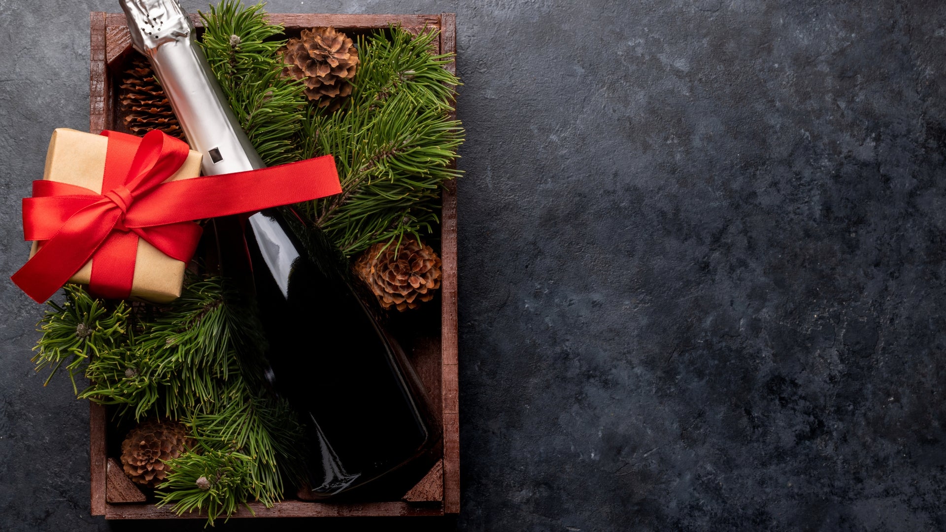 Bottle of champagne with a red bow and pine branches on a dark surface