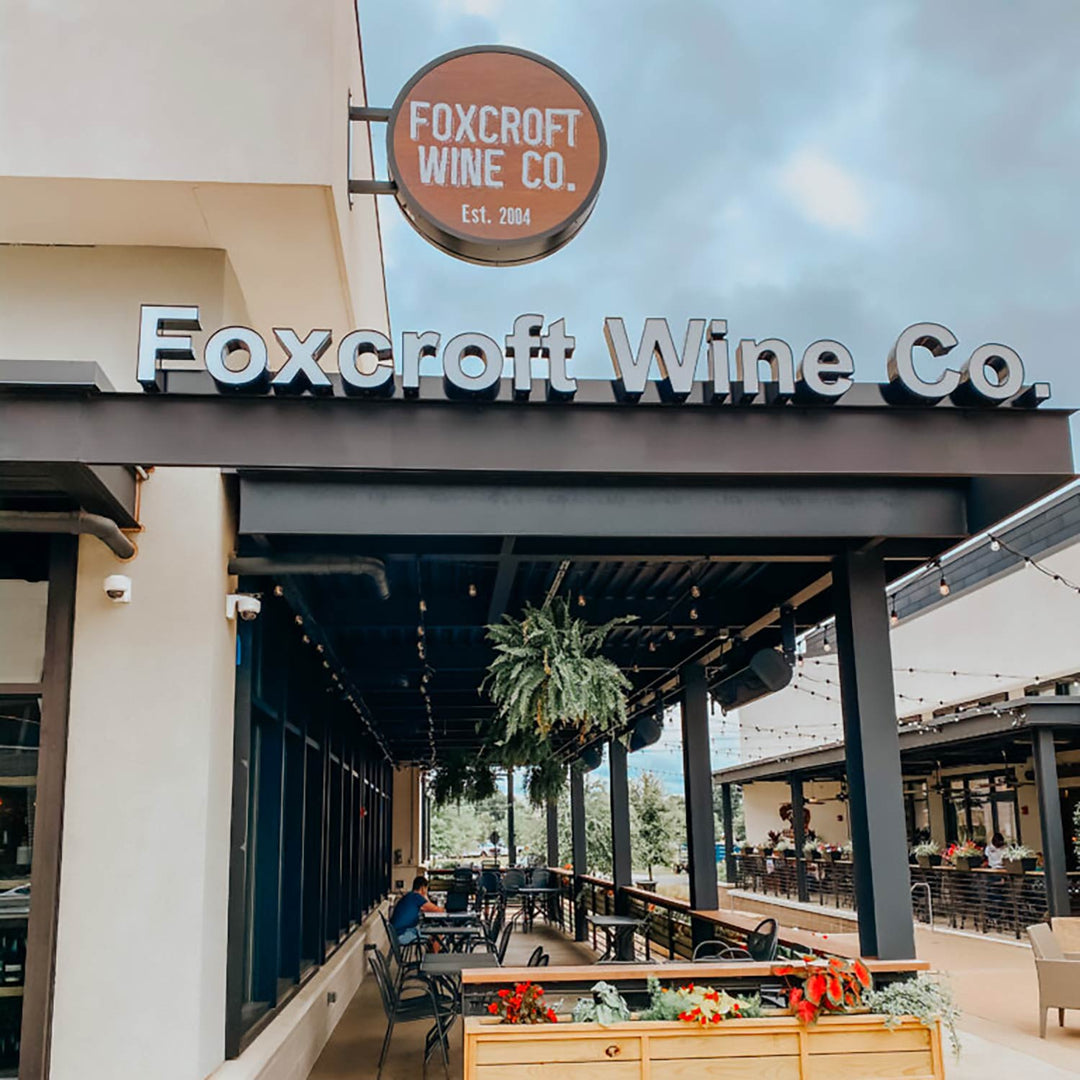 Foxcroft Wine Co. sign above a long covered patio with outdoor tables lined with flower boxes and string lights.