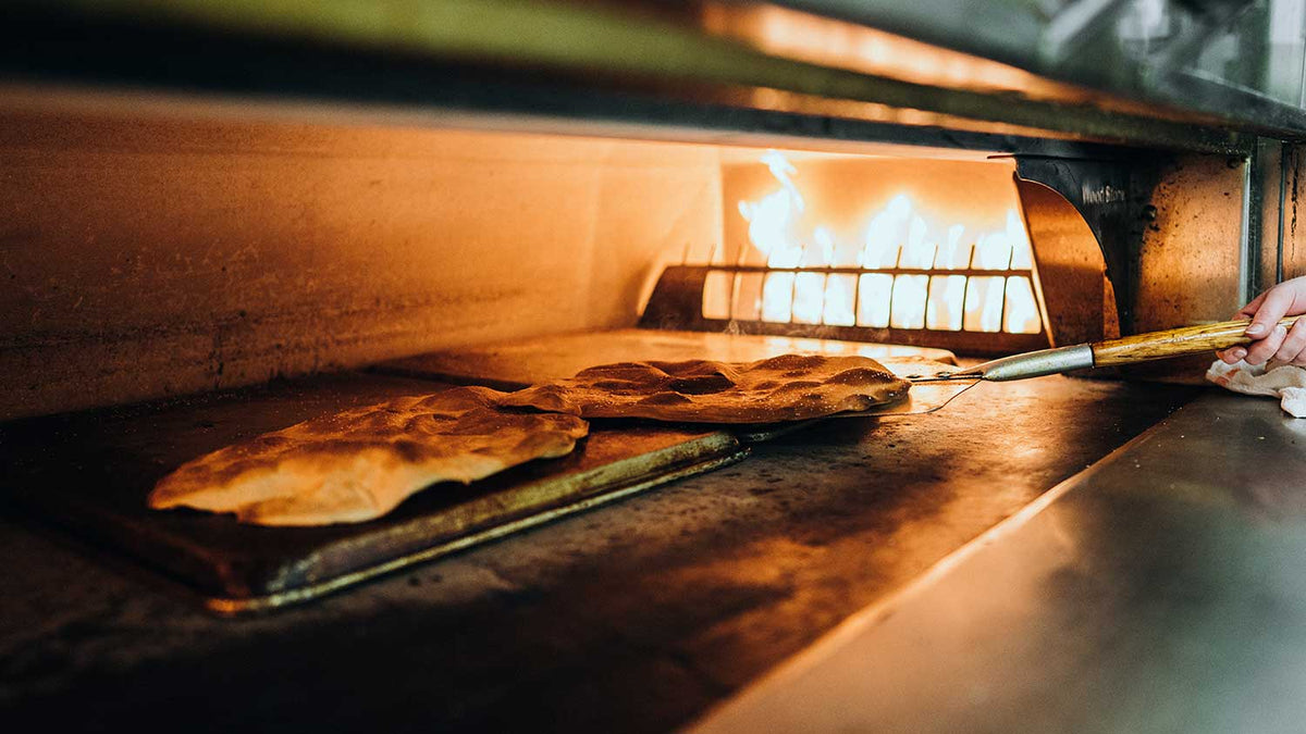 Chef rearranging flatbreads in the oven with fire in the background