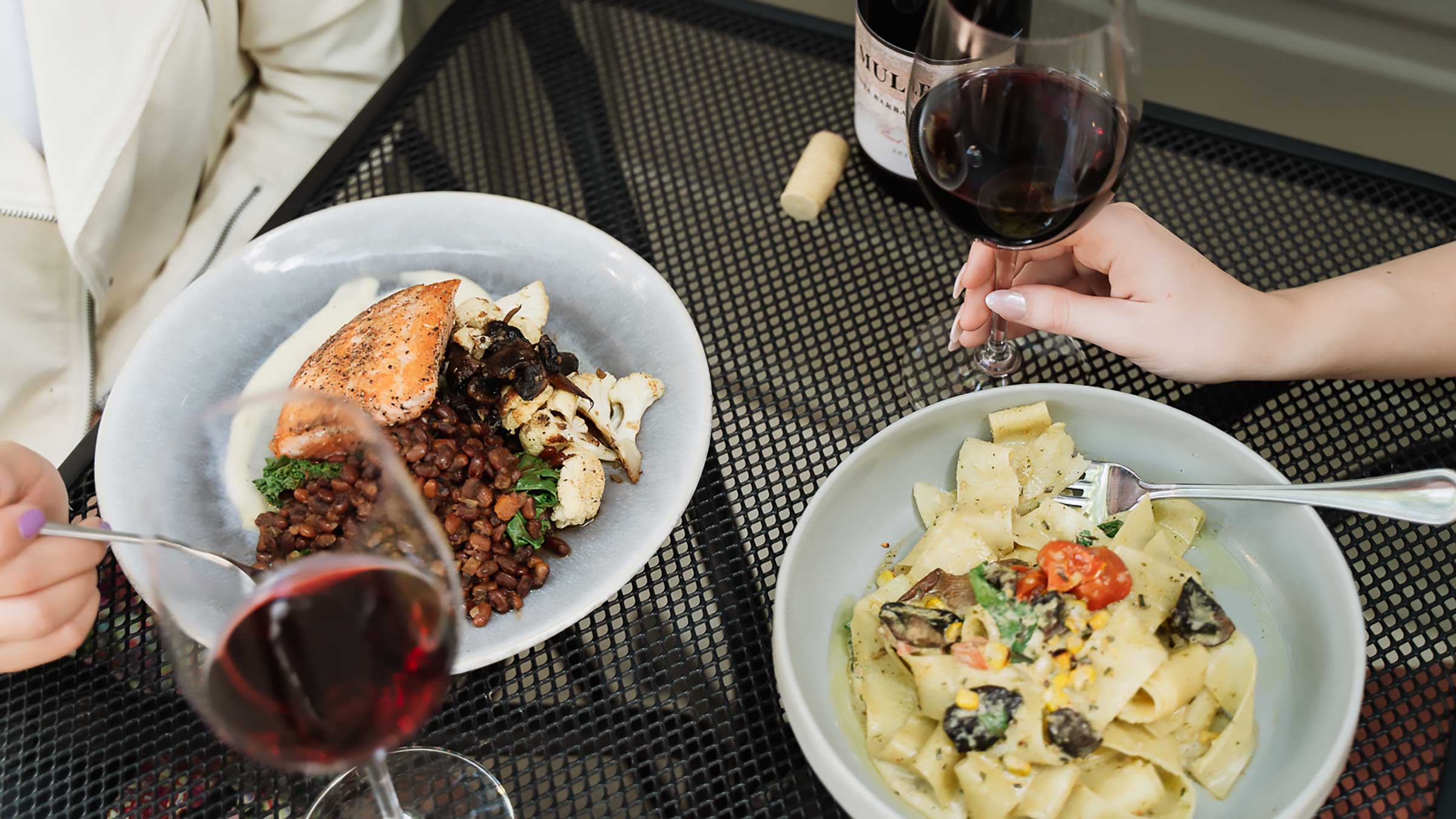 Woman holding a glass of red wine next to a bowl of house-made pasta at an outdoor table