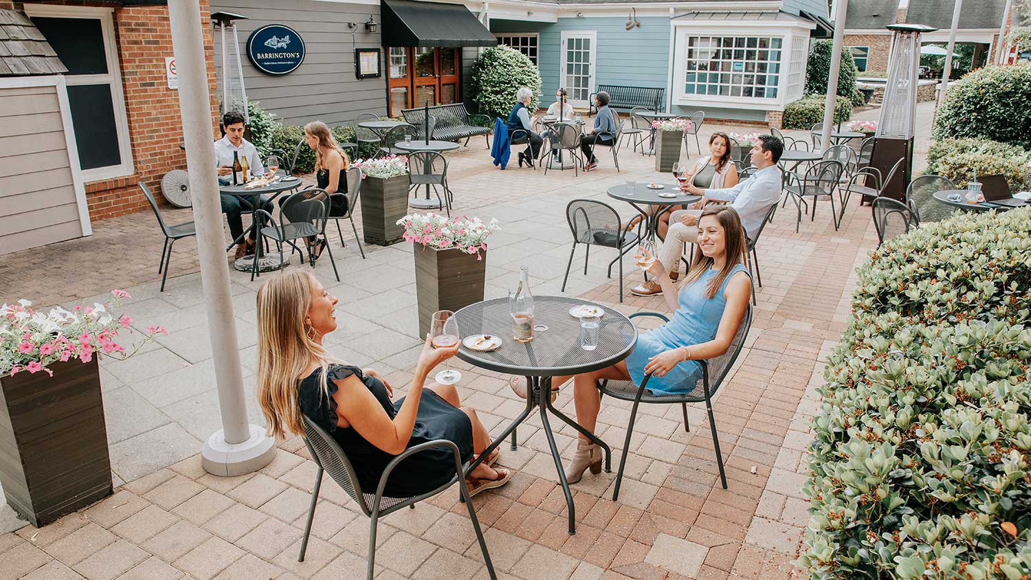 Several tables of customers enjoying small plates and bottles of wine on Foxcroft SouthPark's outdoor patio