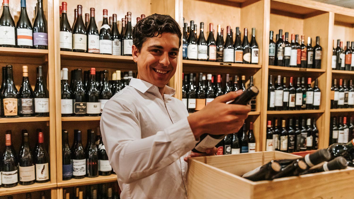 Smiling customer holding a bottle of wine in the wine shop section of Foxcroft SouthPark.