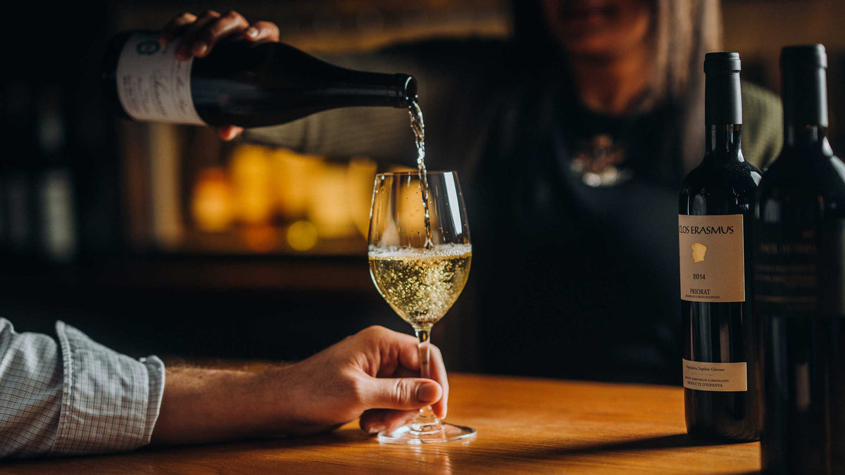 White wine poured by a server behind a standing bar into a glass held by a party guest in the foreground.