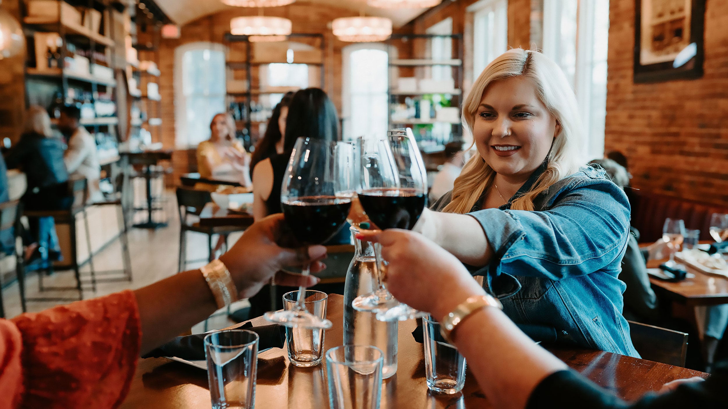 Three women raising their glasses of red wine at a hightop table