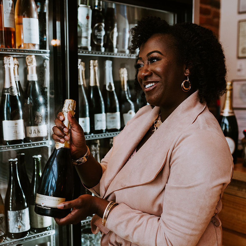 Sommelier displaying a bottle in front of the wine shop fridge.